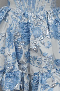 A close-up view of a luxurious mini dress featuring intricate blue floral jacquard fabric, showcasing detailed embroidery and a ruffled hem.
