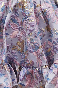 Close-up view of a luxurious lilac mini dress featuring intricate floral jacquard patterns in pink, blue, and gold.