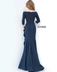 A woman stands with her back to the camera, wearing a sleek navy gown with off-the-shoulder sleeves and a fishtail hem.