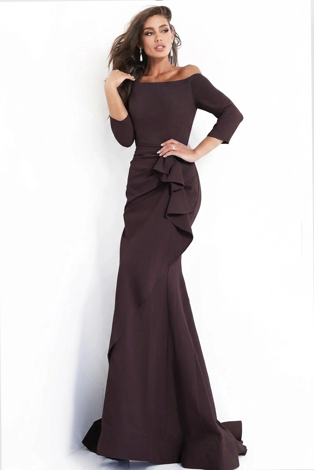 A model poses in a stunning plum gown featuring an off-the-shoulder neckline and elegant ruffle details, perfect for a black tie wedding or gala.