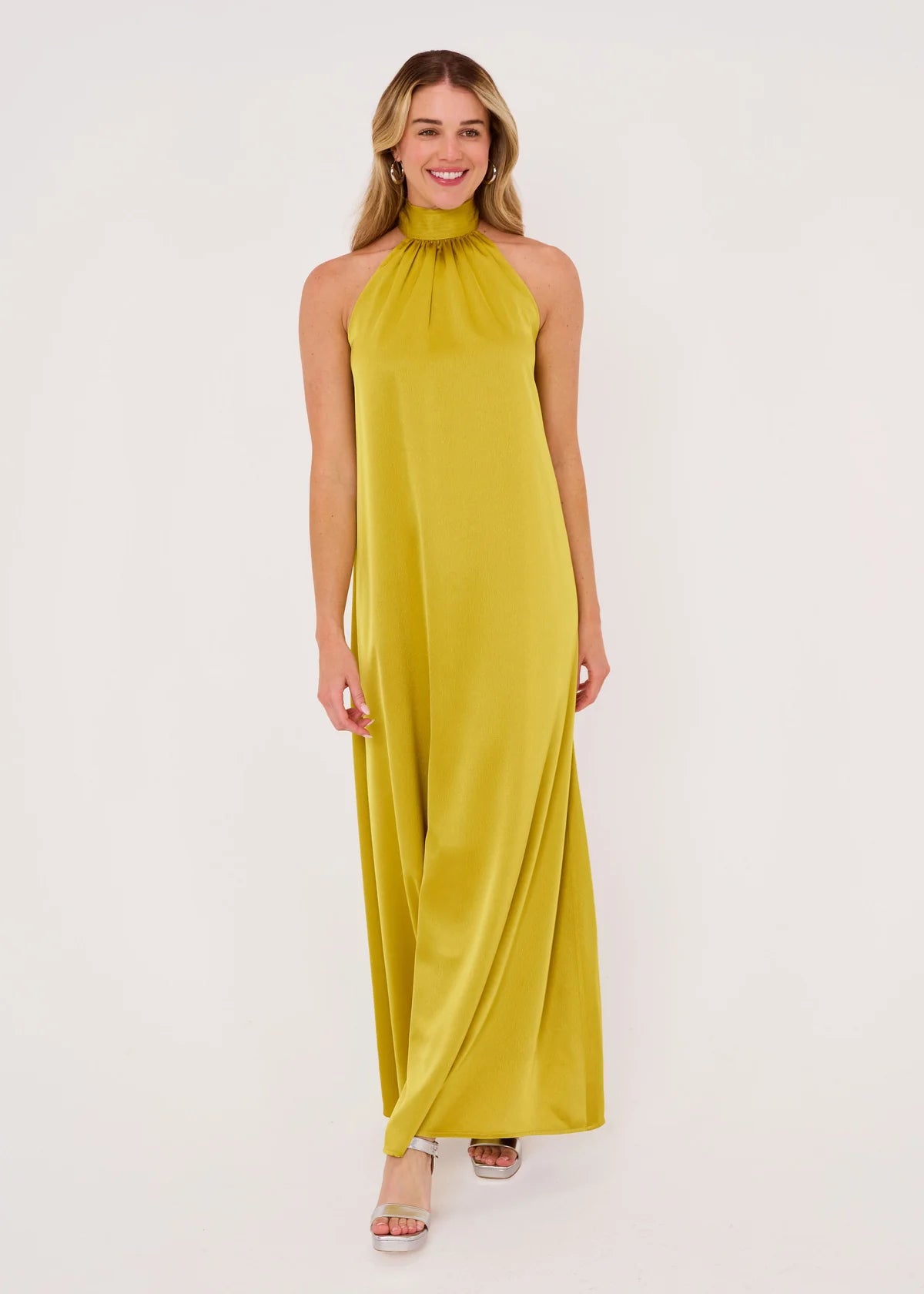A model showcases a full-length gown in a rich golden olive satin, featuring a high neckline and a flowing silhouette.