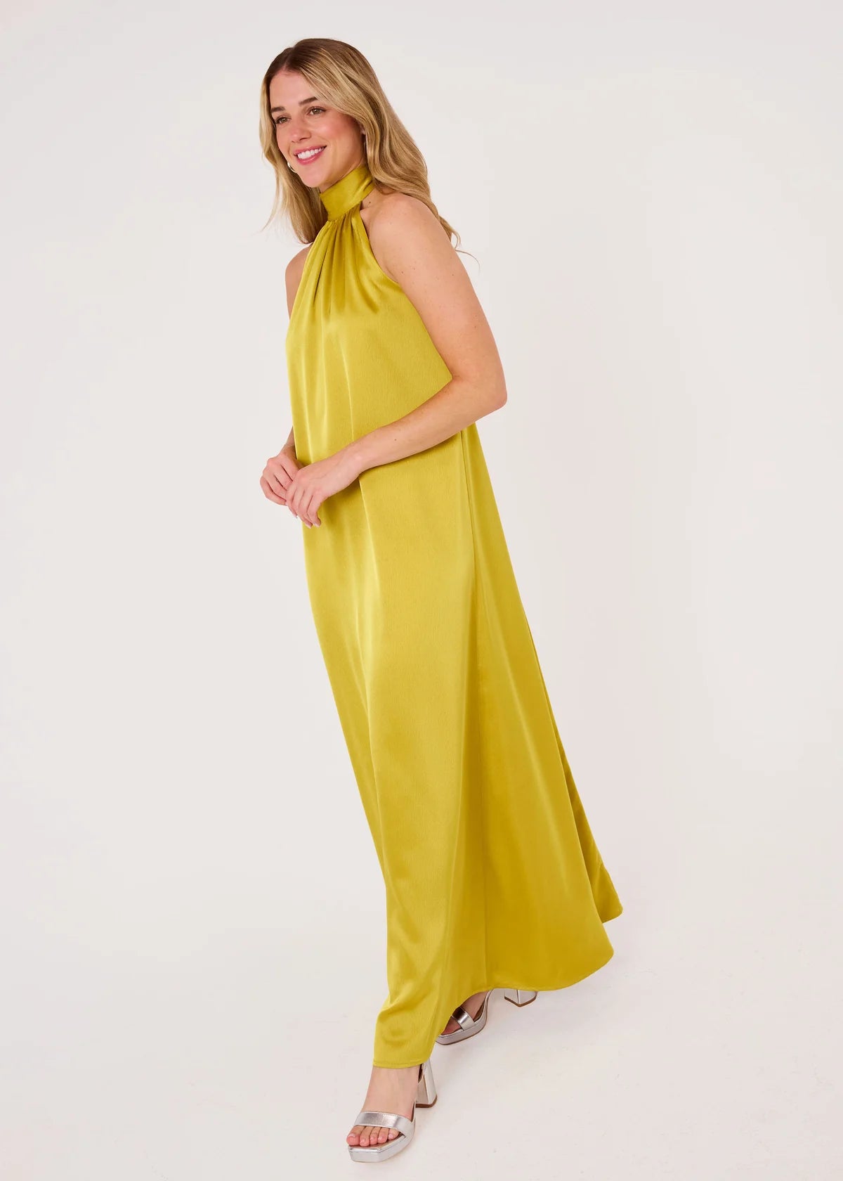 A model poses in a full-length golden olive satin gown with a high neckline and elegant bow-tie detail.