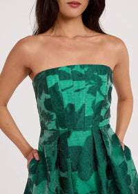 A model showcases a strapless emerald green dress featuring a structured bodice with pleats and a floral pattern.