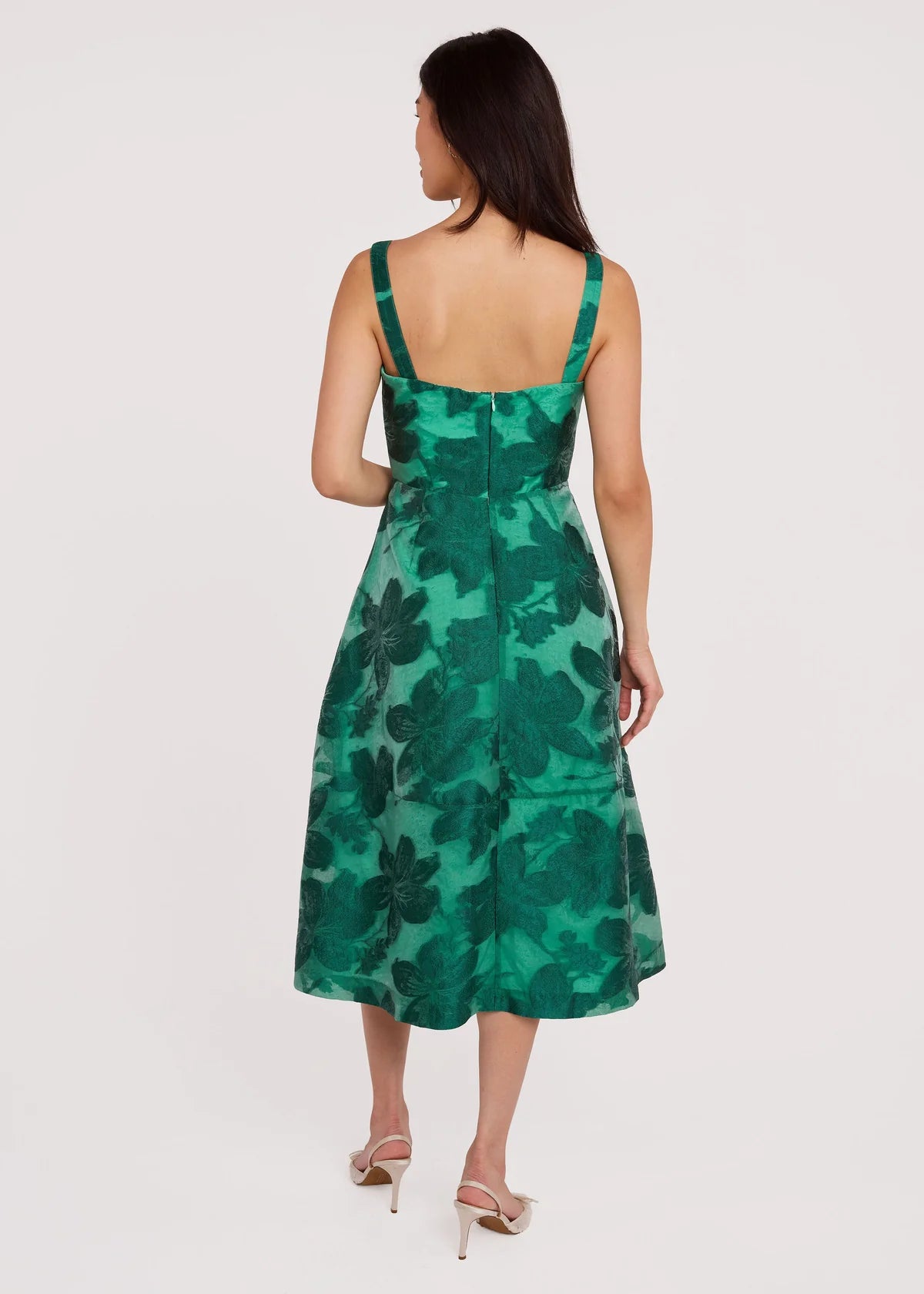 A model showcases the Catherine Dress in a vibrant green floral pattern, featuring a structured bodice and a mid-length skirt.
