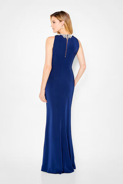 A woman is shown from the back wearing a sleek navy A-line gown with a high neckline and elegant embellishments at the collar.