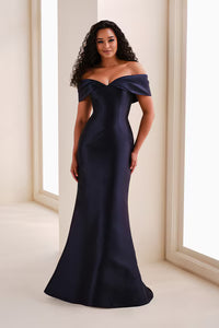 A model poses in an elegant off-the-shoulder navy mikado trumpet gown featuring a pleated V-neckline and fold-over back detail.