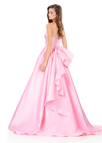 A model showcases a stunning, strapless ice pink gown featuring a voluminous skirt and a large bow at the back, perfect for formal events like proms, galas, or weddings. This elegant dress is available near Apex, Cary, and Raleigh.