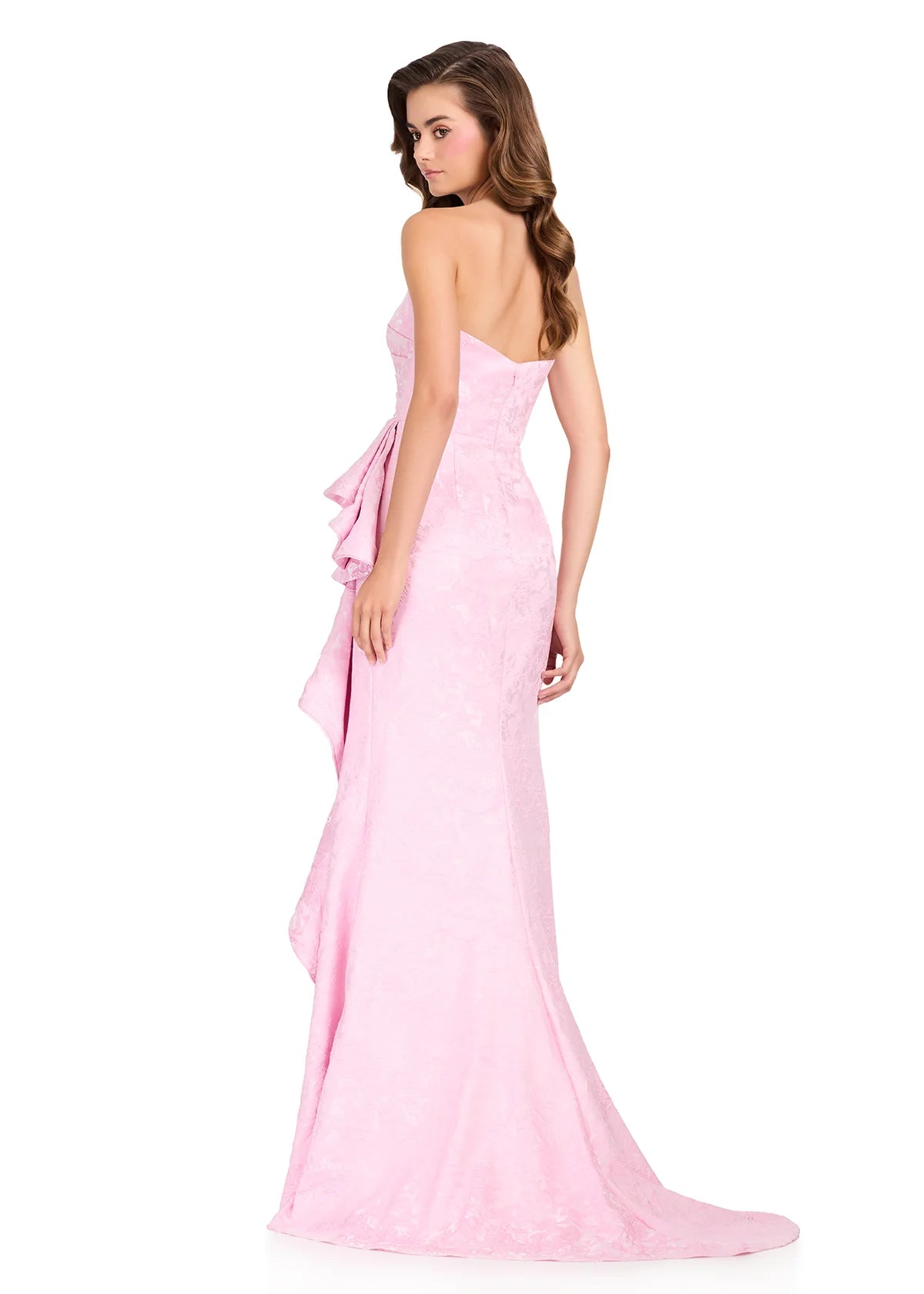 A model showcases a stunning strapless ice pink brocade gown featuring a structured bodice and soft ruching, ideal for elegant occasions such as prom or a black tie wedding. This dress is conveniently available near Apex, Cary, and Raleigh.