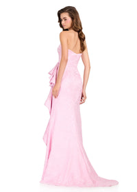 A model showcases a stunning strapless ice pink brocade gown featuring a structured bodice and soft ruching, ideal for elegant occasions such as prom or a black tie wedding. This dress is conveniently available near Apex, Cary, and Raleigh.