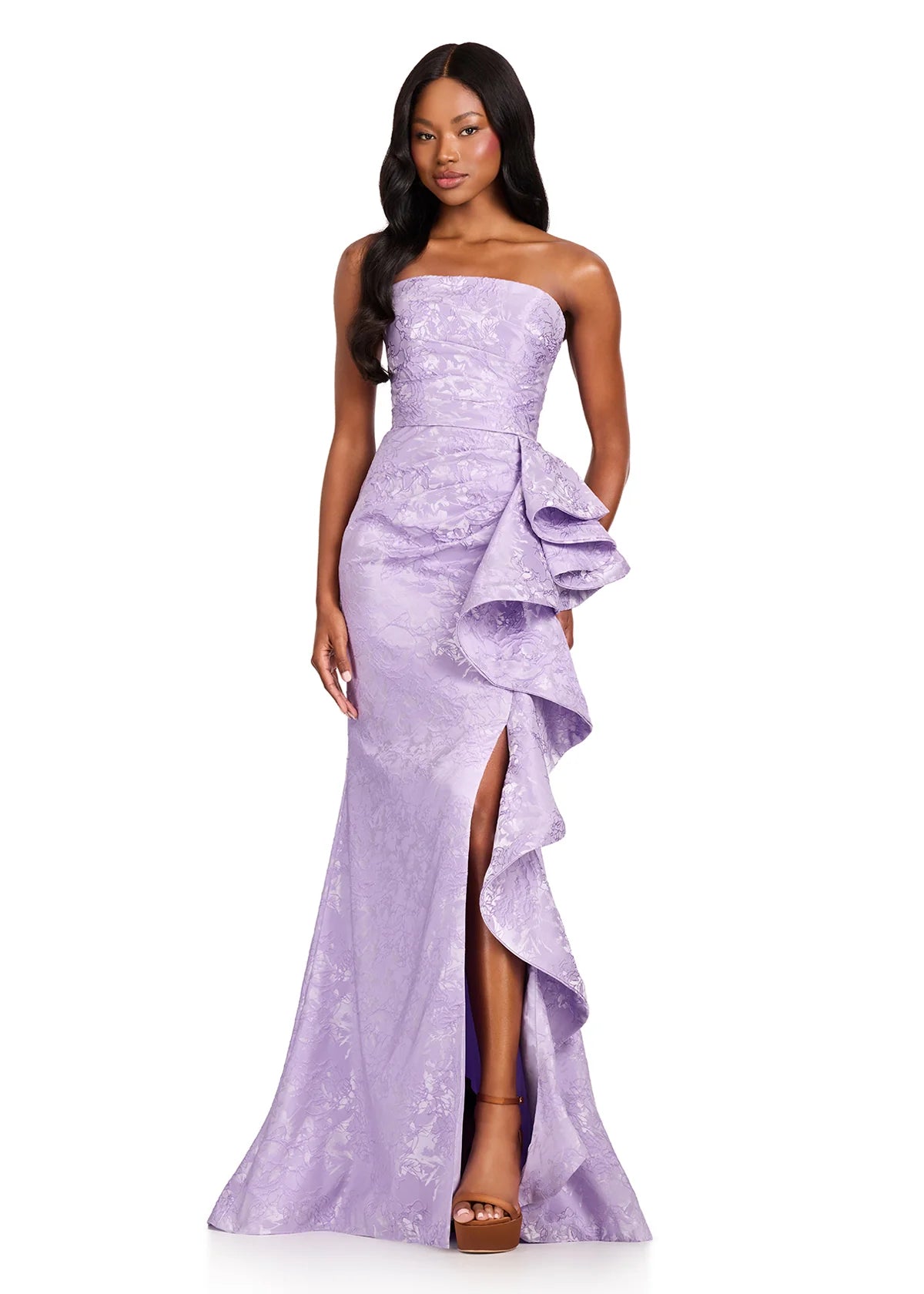 A model showcases an elegant lilac strapless brocade gown with a structured bodice and a cascading ruffle detail.