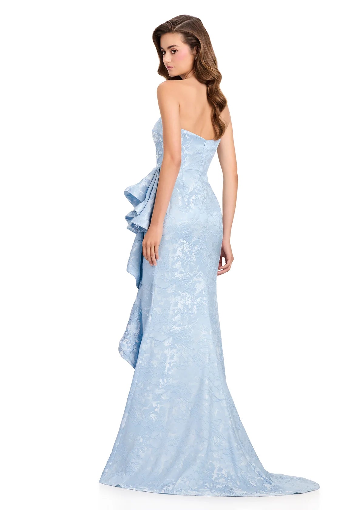 A woman models a stunning strapless light blue brocade gown featuring a structured bodice and elegant cascading ruffles at the back.