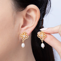 A close-up image of a woman wearing elegant flower filigree pearl drop earrings, featuring intricate gold detailing and a delicate pearl drop. These stylish earrings are perfect for special occasions like weddings or galas.