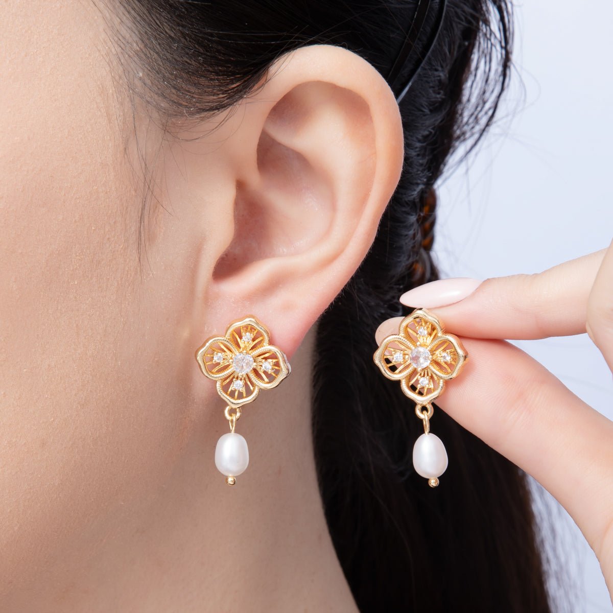 A close-up image of a woman wearing elegant flower filigree pearl drop earrings, featuring intricate gold detailing and a delicate pearl drop. These stylish earrings are perfect for special occasions like weddings or galas.