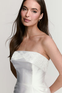 A model showcases a strapless white gown with intricate beading along the neckline, exuding elegance. This dress is perfect for special occasions such as weddings, galas, or formal events, and is conveniently available near Apex,.