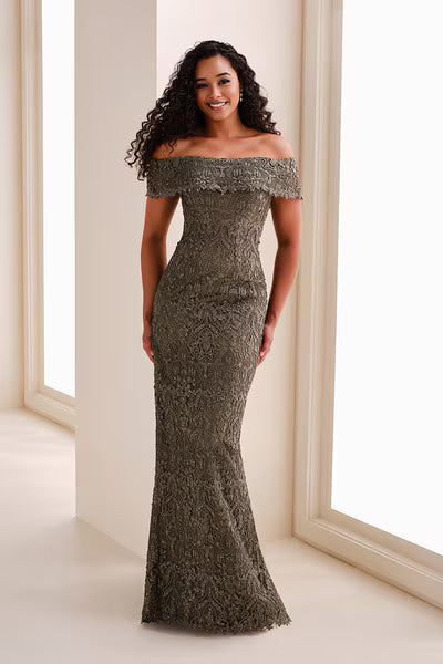 A model stands elegantly in an off-the-shoulder allover lace sheath gown in olive green, showcasing a straight neckline and fitted silhouette.