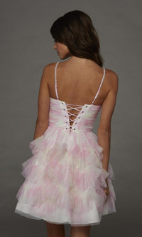 A young woman stands with her back to the camera, showcasing a pink and white ruffled dress with a lace-up detail. This playful gown is perfect for events like prom, homecoming, or casual gatherings near Apex, Cary, and Raleigh.