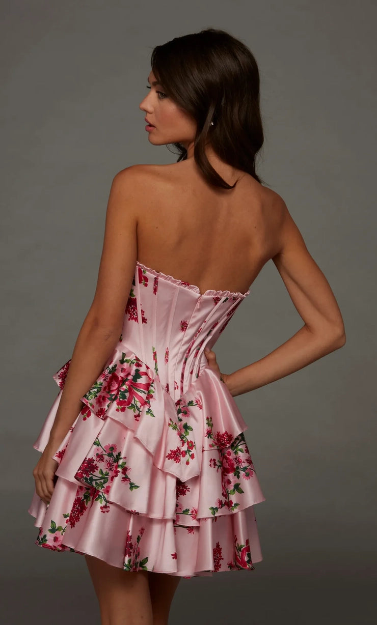 A young woman is shown from the back in a strapless pink dress adorned with floral patterns and layered ruffles.
