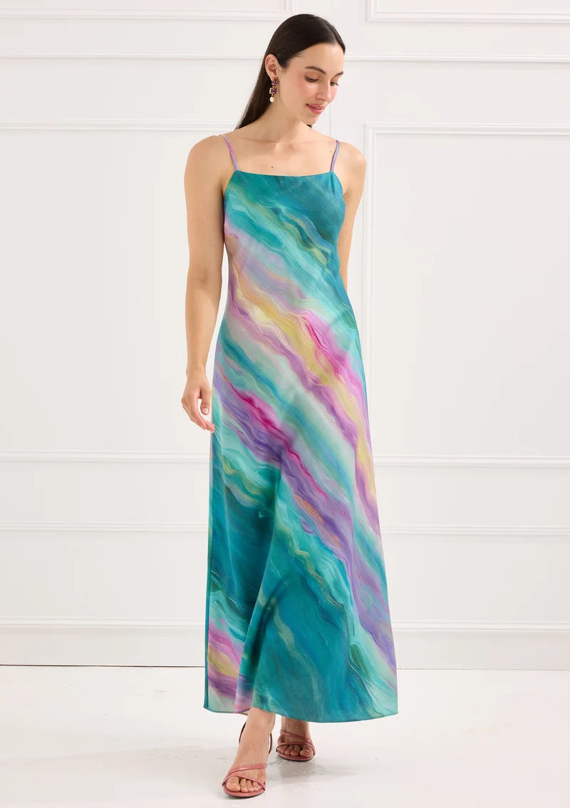 A woman models a long, flowing dress featuring a vibrant, multicolored wave pattern in shades of blue, pink, and purple. This elegant dress is perfect for special occasions like proms or gala events, available near Apex, Cary, and Raleigh.