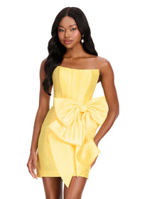 A model showcases a stunning yellow strapless dress featuring a large bow accent and a fitted silhouette. Perfect for mother of the bride, prom, or gala events, this elegant gown is conveniently located near Apex, Cary, and Raleigh.