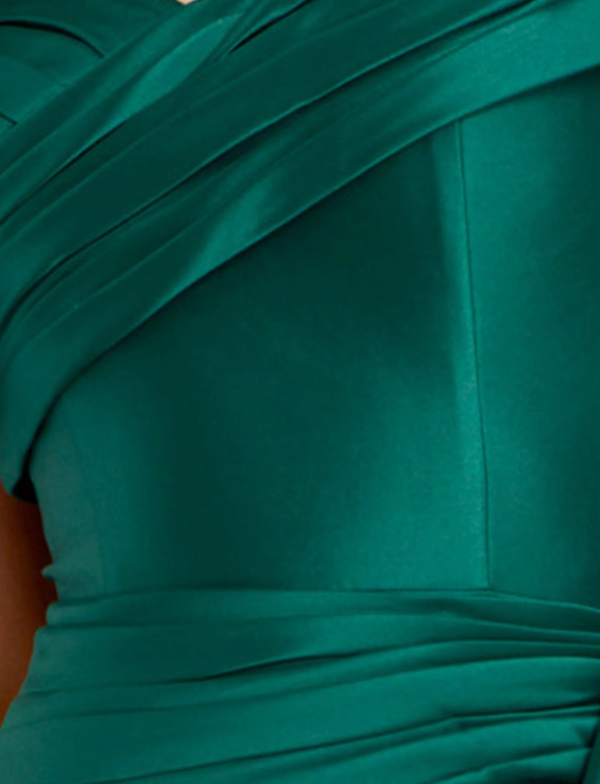 Close-up of a luxurious emerald green gown featuring intricate pleats that create an elegant texture. Ideal for special occasions like proms or galas, this dress is conveniently available near Apex, Cary, and Raleigh.