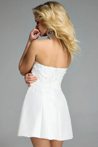 A model poses in a strapless off-white dress with intricate floral detailing on the back, showcasing a fitted bodice and a flared skirt.