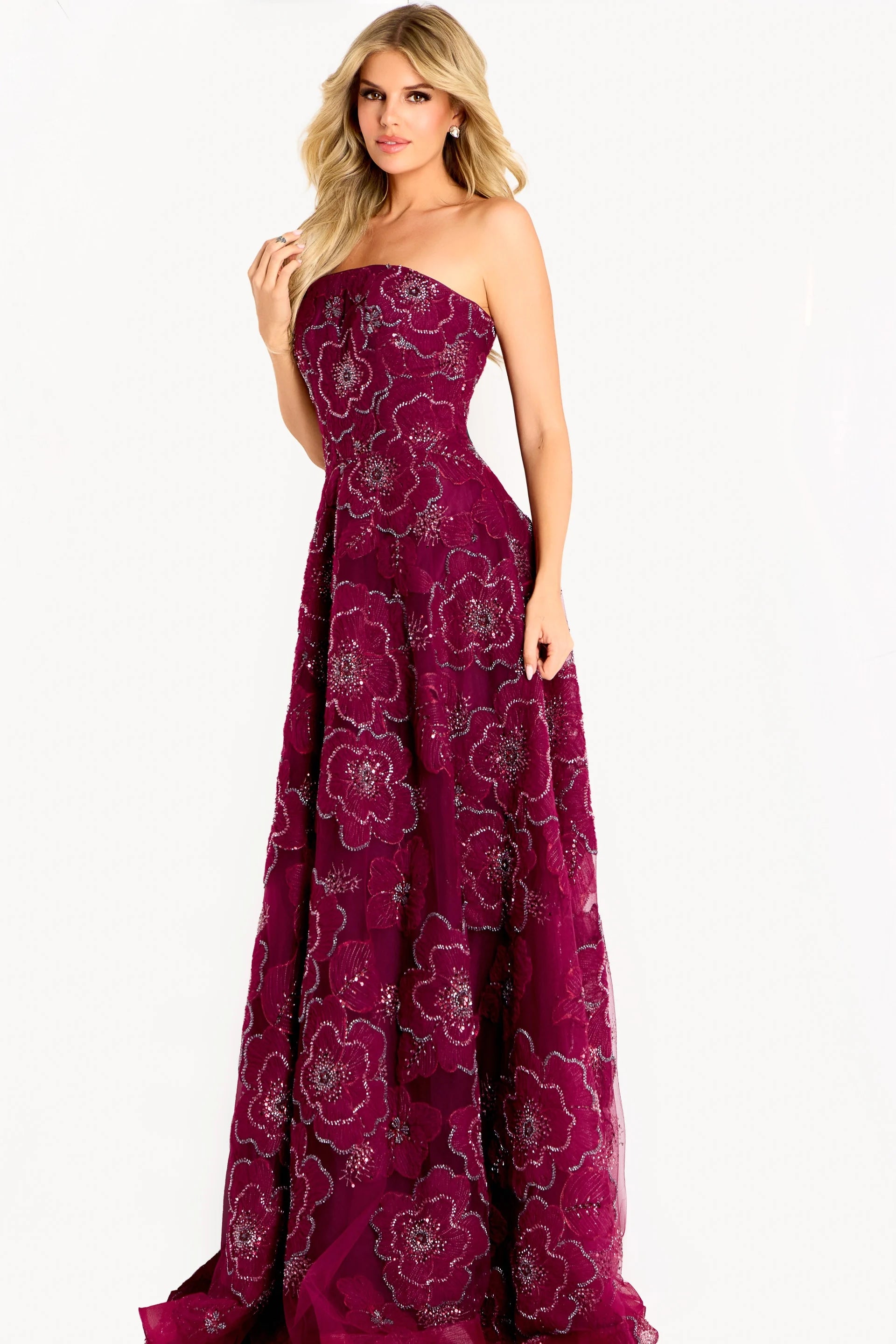 A model showcases a stunning burgundy strapless A-line gown adorned with floral appliqué details and a layered skirt.