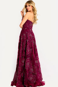 A model showcases a stunning burgundy strapless A-line gown with intricate floral embroidery and a layered skirt.