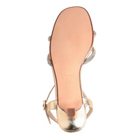 The image shows the underside of a gold strappy sandal with a smooth, shiny surface and delicate embellishments.
