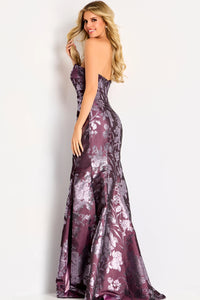 A model poses in a stunning strapless burgundy gown adorned with intricate floral patterns, showcasing a fitted silhouette that flares at the bottom.