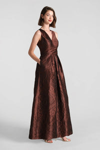 A model showcases the elegant Mariah Gown in rich chocolate brown, featuring a textured jacquard fabric and a sophisticated silhouette with pockets.