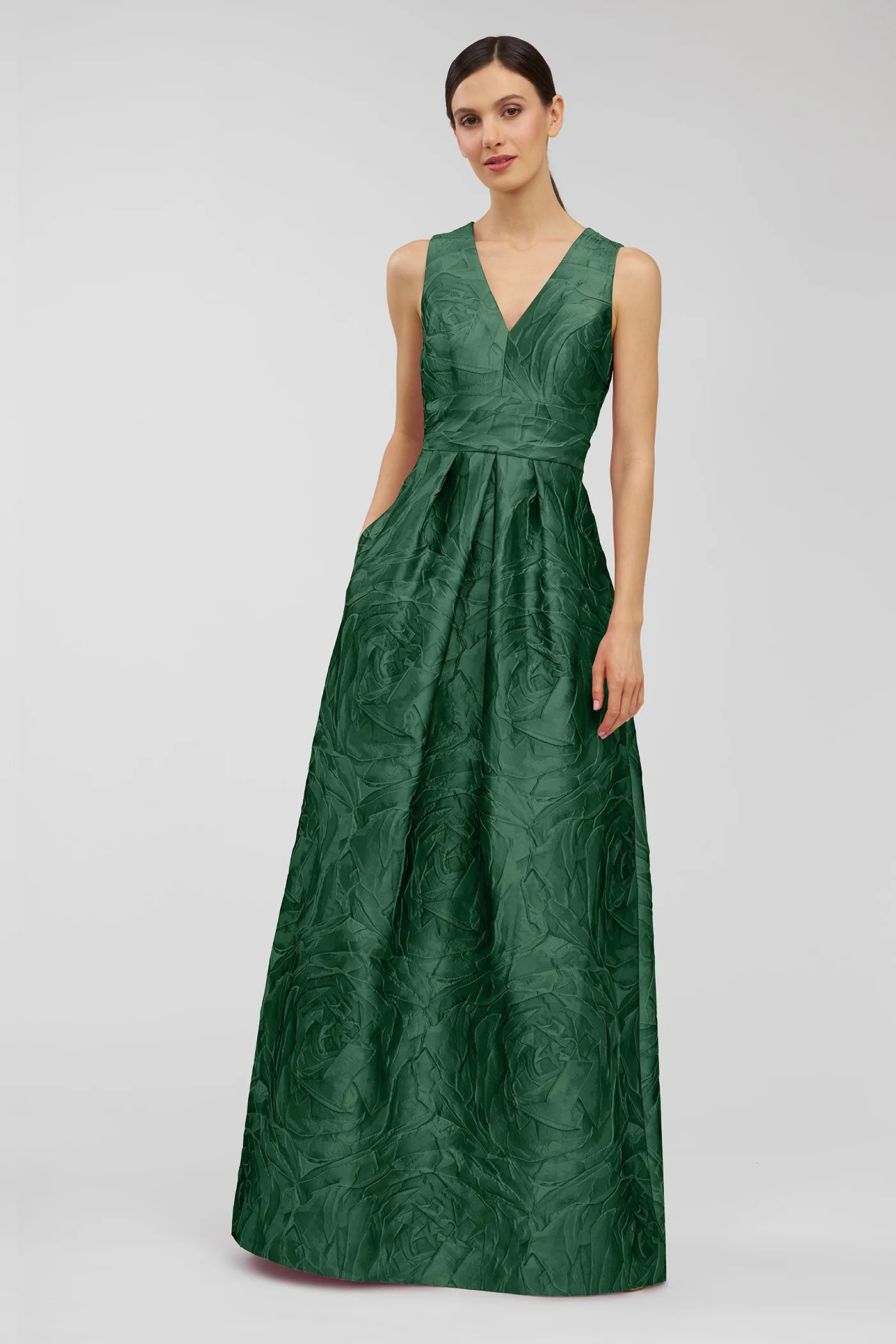 A model showcases the elegant Mariah Gown in a rich emerald green, featuring a deep V-neck and textured jacquard fabric with floral patterns.