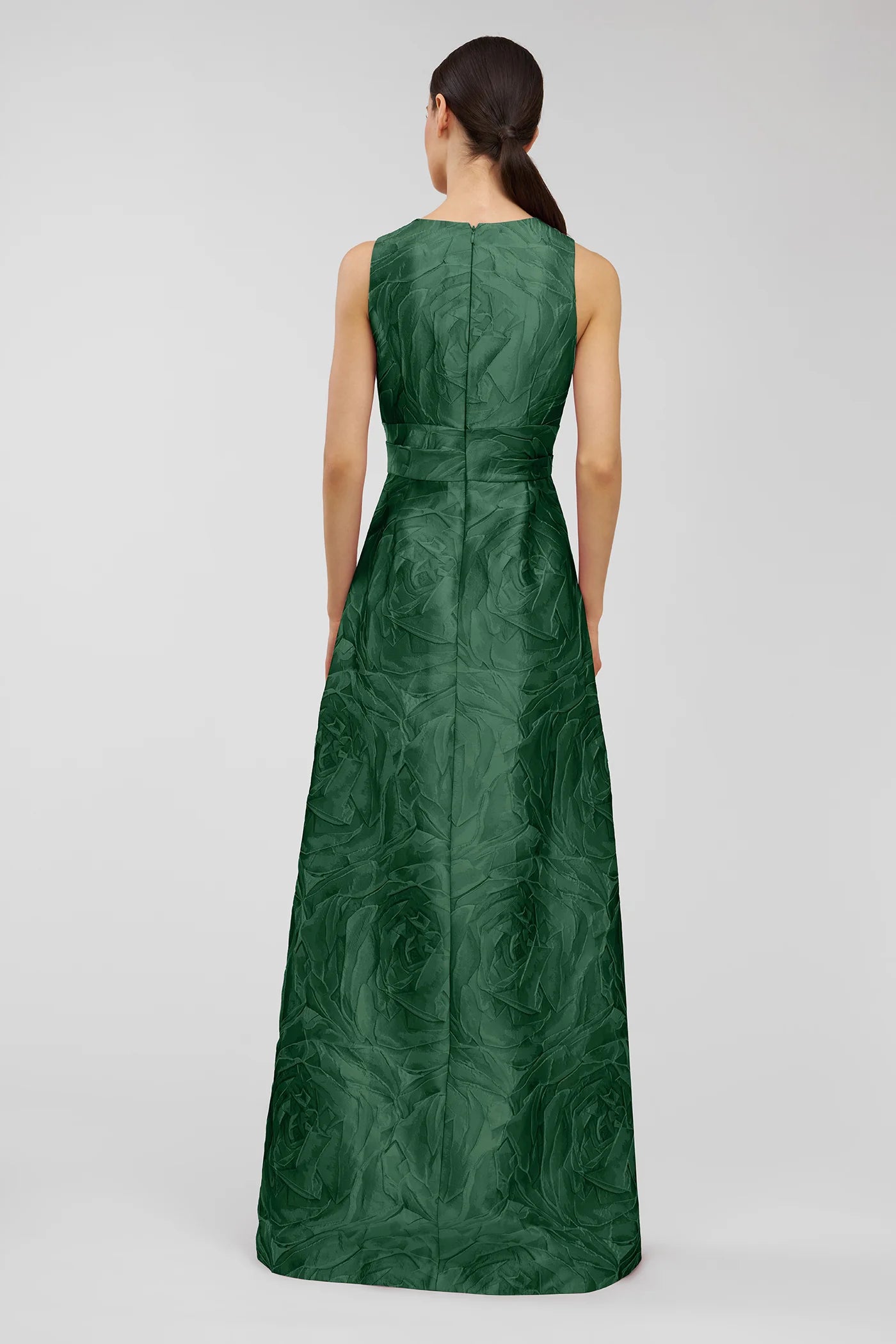 A model showcases the elegant Mariah Gown in a rich emerald green, featuring a textured jacquard design. Ideal for formal events like galas or black tie weddings, this stunning dress is conveniently available near Apex, Cary, and Raleigh.