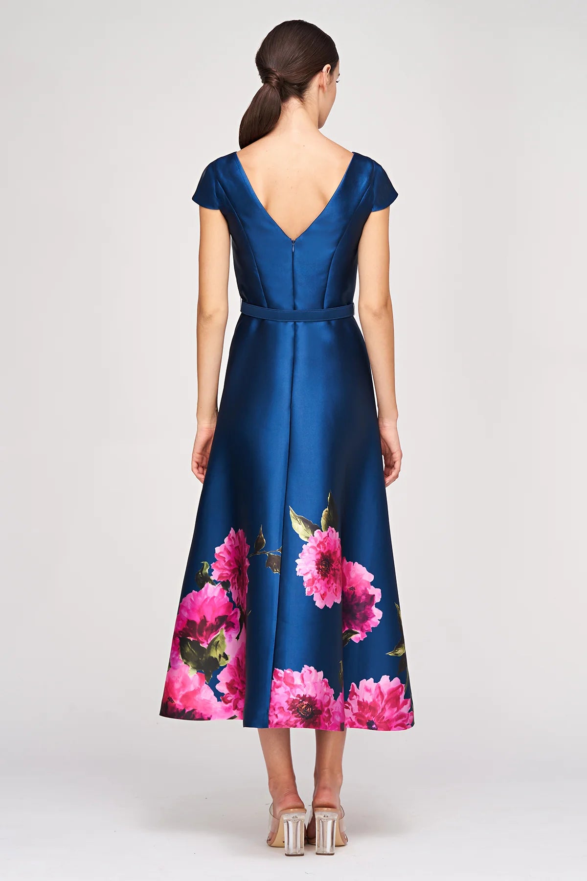 A model showcases a beautiful navy blue gown featuring short cap sleeves and a flattering V-back. The dress is adorned with vibrant pink floral details along the hem, making it perfect for events like weddings or galas in the Apex,.