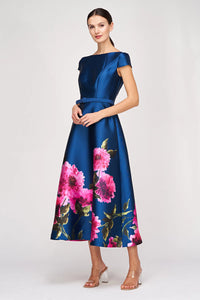 A model poses in a stunning blue satin gown adorned with vibrant pink floral patterns. This elegant dress is perfect for special occasions like weddings, galas, or proms, and is conveniently located near Apex, Cary, and Raleigh.