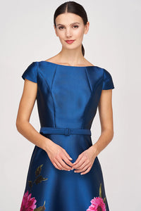 A model is wearing a stunning blue satin gown featuring elegant floral designs and a fitted bodice with cap sleeves.