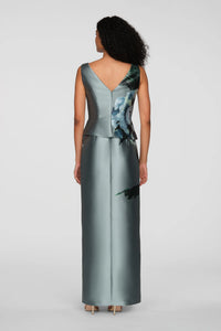 A woman is seen from the back wearing a sleek, floor-length gown with a V-neck and an asymmetrical peplum featuring a floral print.