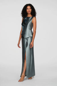A model showcases a sleek, floor-length gown in a soft teal hue with an asymmetrical peplum detail and a front slit.