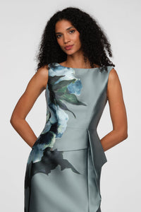 A woman poses confidently in a stylish gown featuring a striking floral design in shades of blue and green.