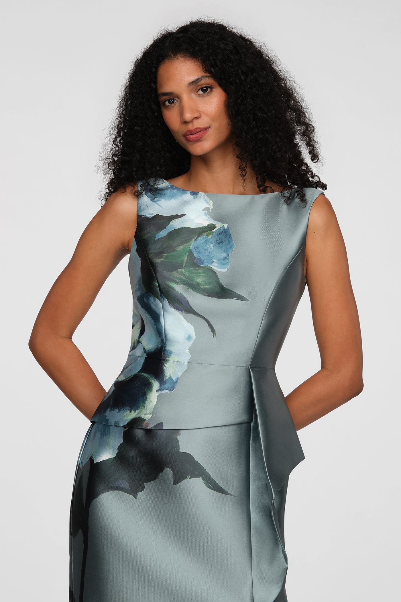 A woman poses confidently in a stylish gown featuring a striking floral design in shades of blue and green.