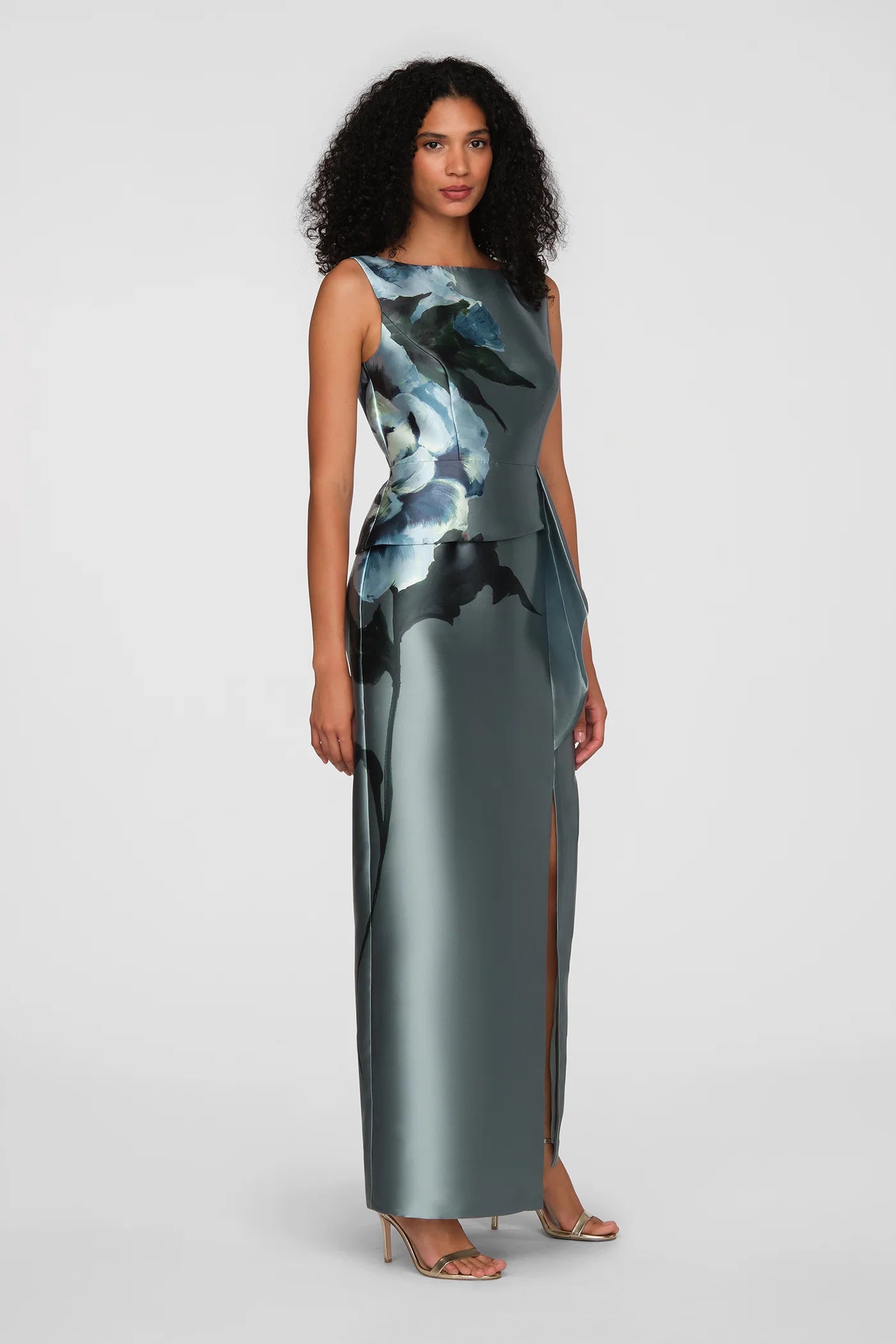 A model showcases an elegant floor-length gown in a sleek column silhouette, featuring an eye-catching floral design and a front slit. Perfect for a black tie wedding or gala, this dress is conveniently located near Apex, Cary, and Raleigh.
