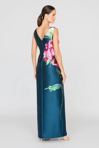 The image features a woman wearing a stunning blue gown with a vibrant floral design on the back, showcasing an asymmetrical peplum and a sleek column silhouette.