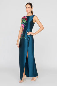 A model poses in a sleek blue satin gown featuring a vibrant rose print and a front slit, perfect for a black tie wedding or gala. This elegant dress is conveniently located near Apex, Cary, and Raleigh for your special occasions.