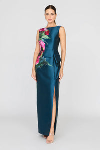 A model showcases a sleek blue gown with a bold floral print and an asymmetrical peplum, featuring a side slit for added elegance.