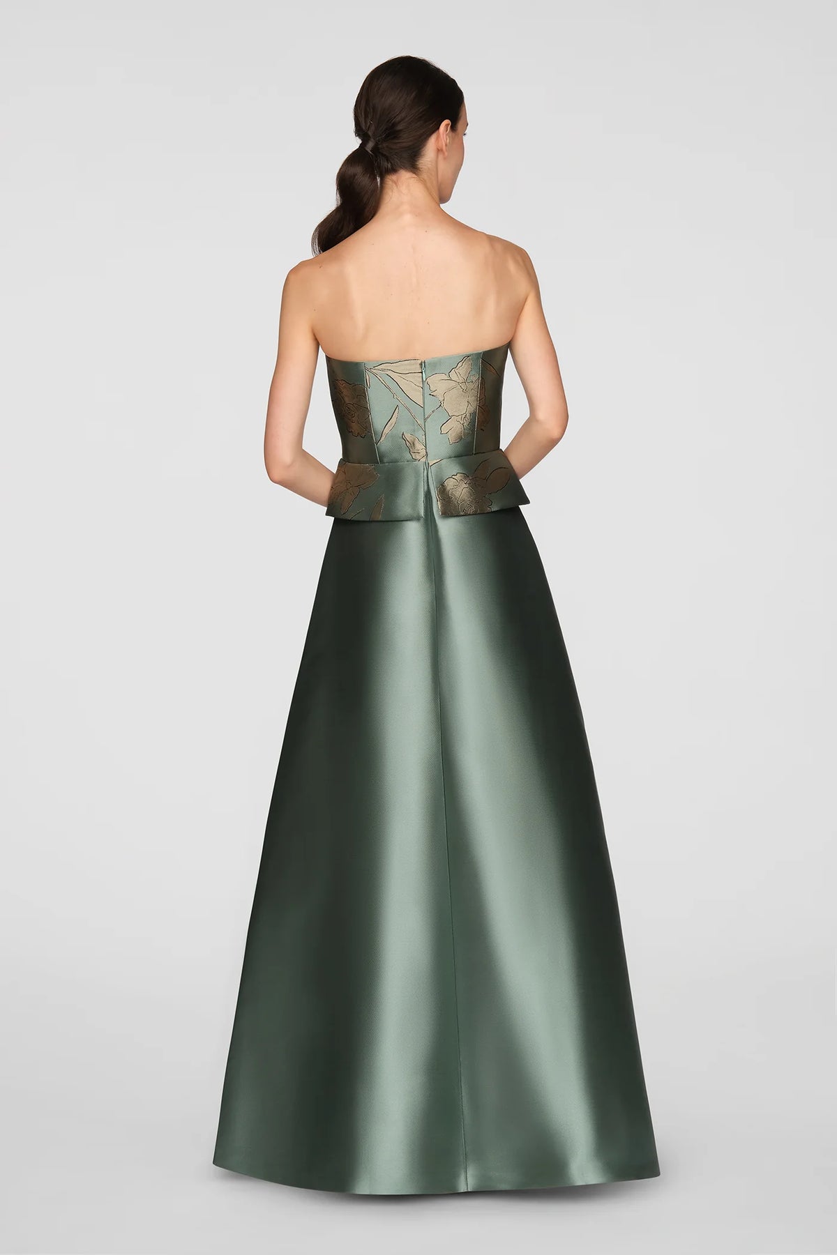 A model showcases a stunning sage green ball gown from the back, featuring a metallic jacquard bodice adorned with gold floral details.