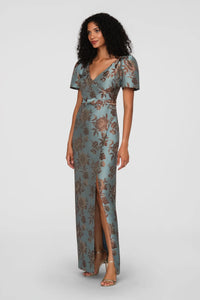 A model showcases a vintage floral jacquard gown in cool blue, featuring a faux-surplice bodice, short sleeves, and a front slit.