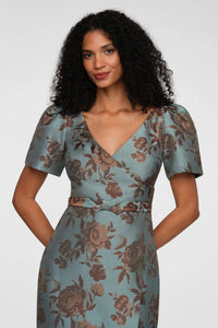 A model showcases a vintage-inspired gown with a cool blue floral jacquard pattern, featuring a faux-surplice bodice and short puff sleeves.