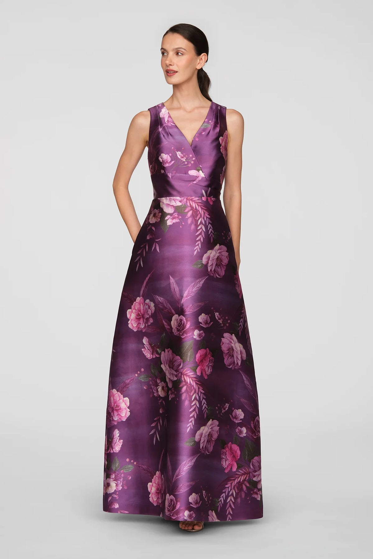 A model showcases a stunning floor-length gown in vivid berry with a rose bouquet print, perfect for formal occasions like a black tie wedding or gala. This elegant dress is conveniently available near Apex, Cary, and Raleigh.