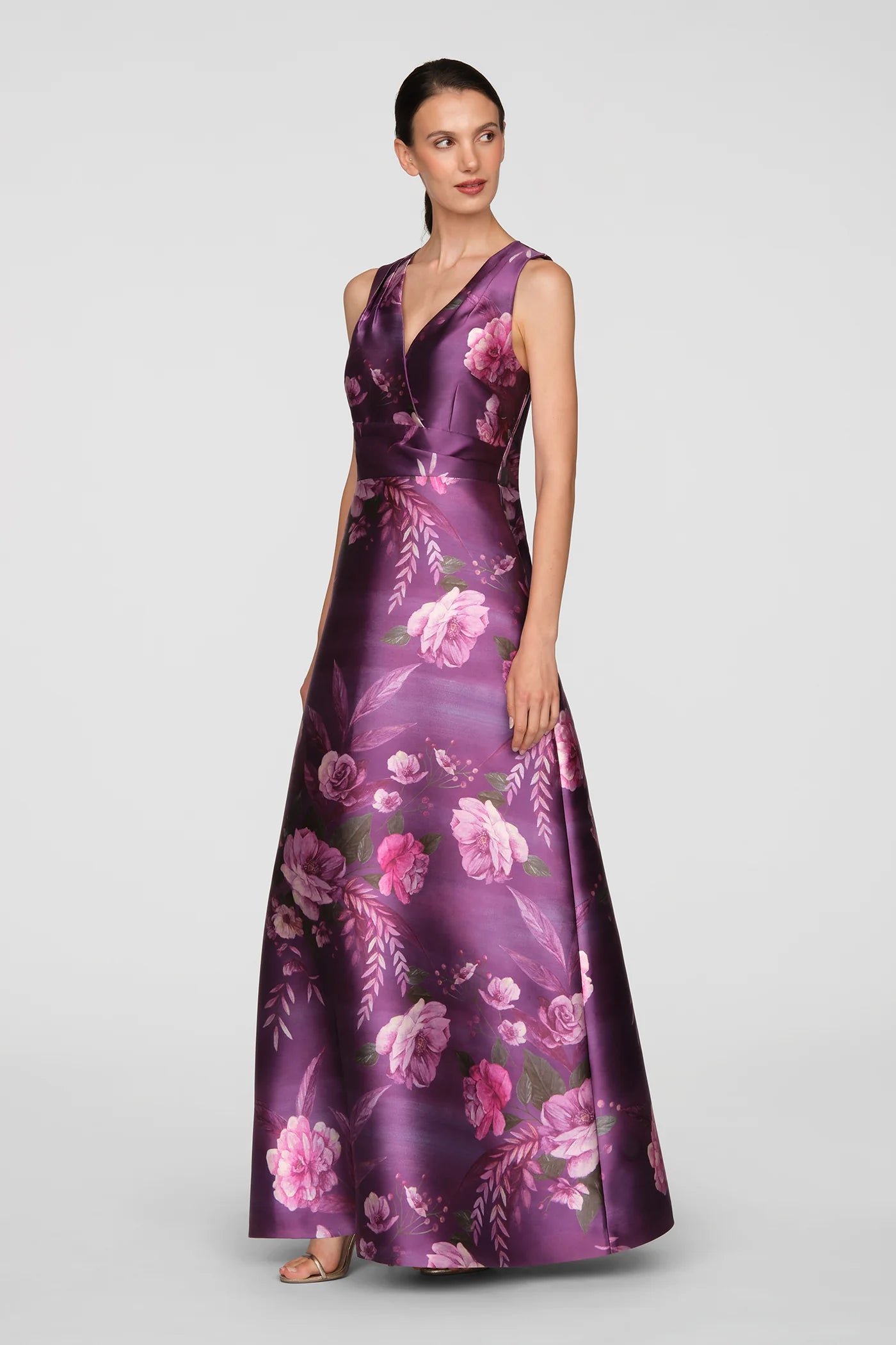 A model showcases a stunning floor-length gown with a vivid berry hue and a vibrant rose bouquet print. This elegant dress is perfect for formal occasions like black tie weddings or galas, conveniently located near Apex, Cary, and Raleigh.