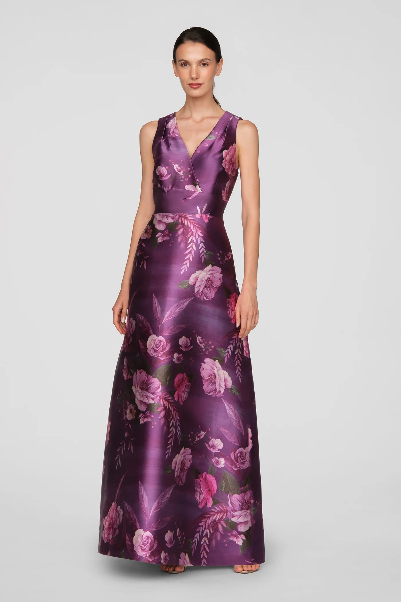 A model showcases a floor-length gown in a vivid berry color adorned with a floral print. This elegant dress is perfect for special occasions such as galas, weddings, or proms, and is conveniently available near Apex, Cary, and Raleigh.