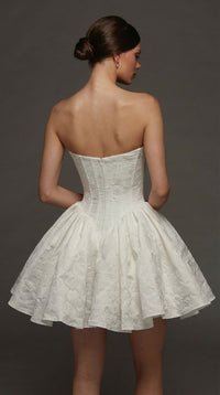 A model is shown from the back wearing a strapless white dress with a fitted bodice and a flared skirt, featuring a textured floral design. This elegant gown is perfect for special occasions like proms, weddings, or gala events.